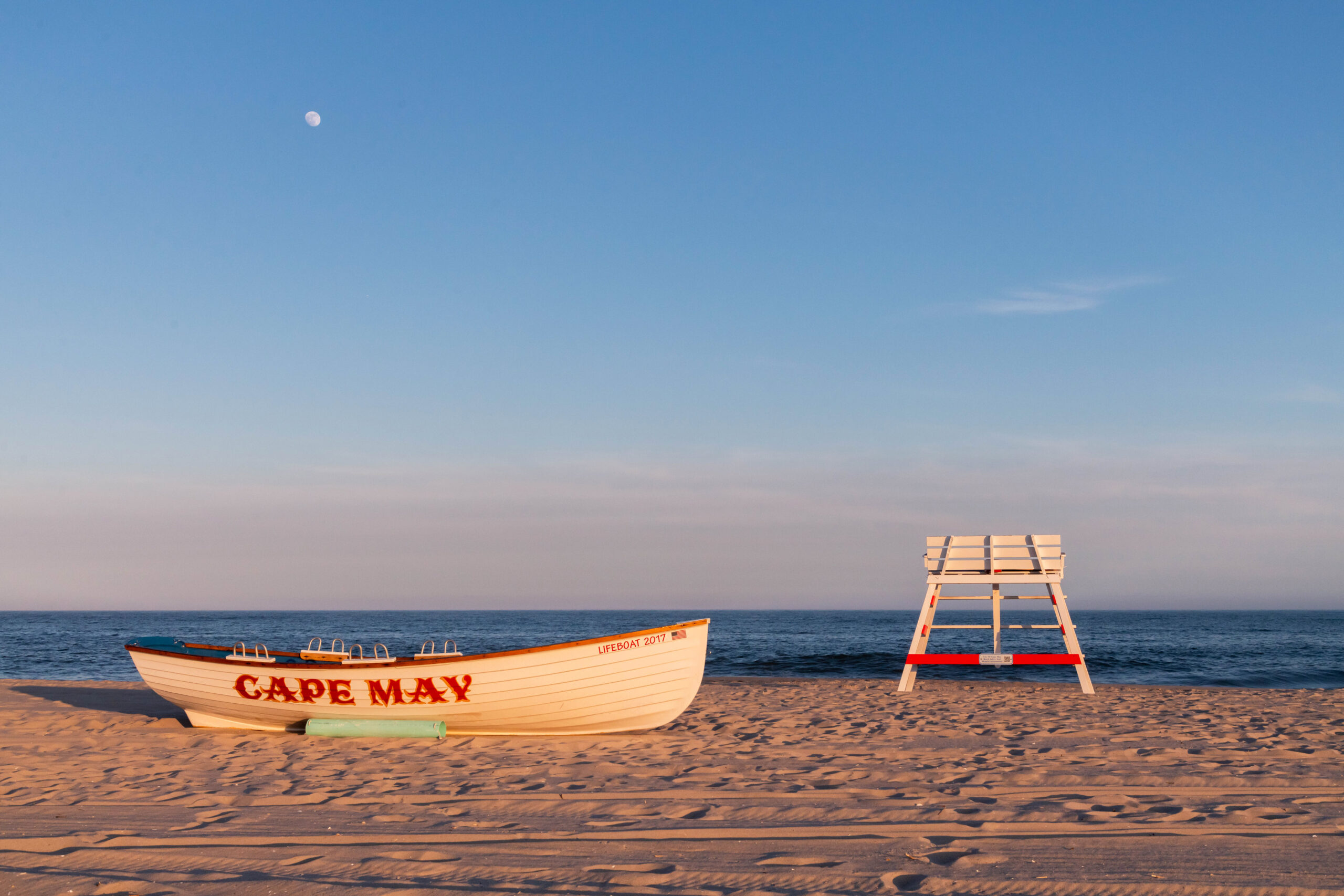A Cape May lifeguard boat and lifeguard stand on the beach at sunset with a full moon in the clear blue sky