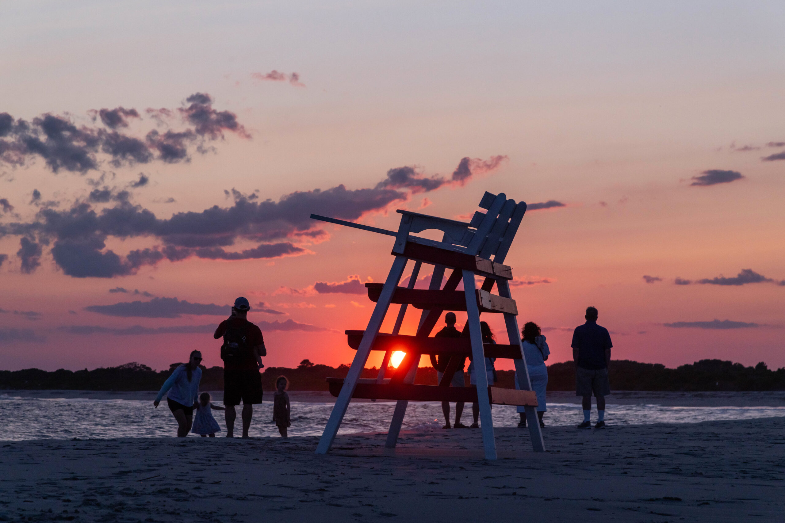A group of people watching a pink sunset around a Cape May lifeguard stand 