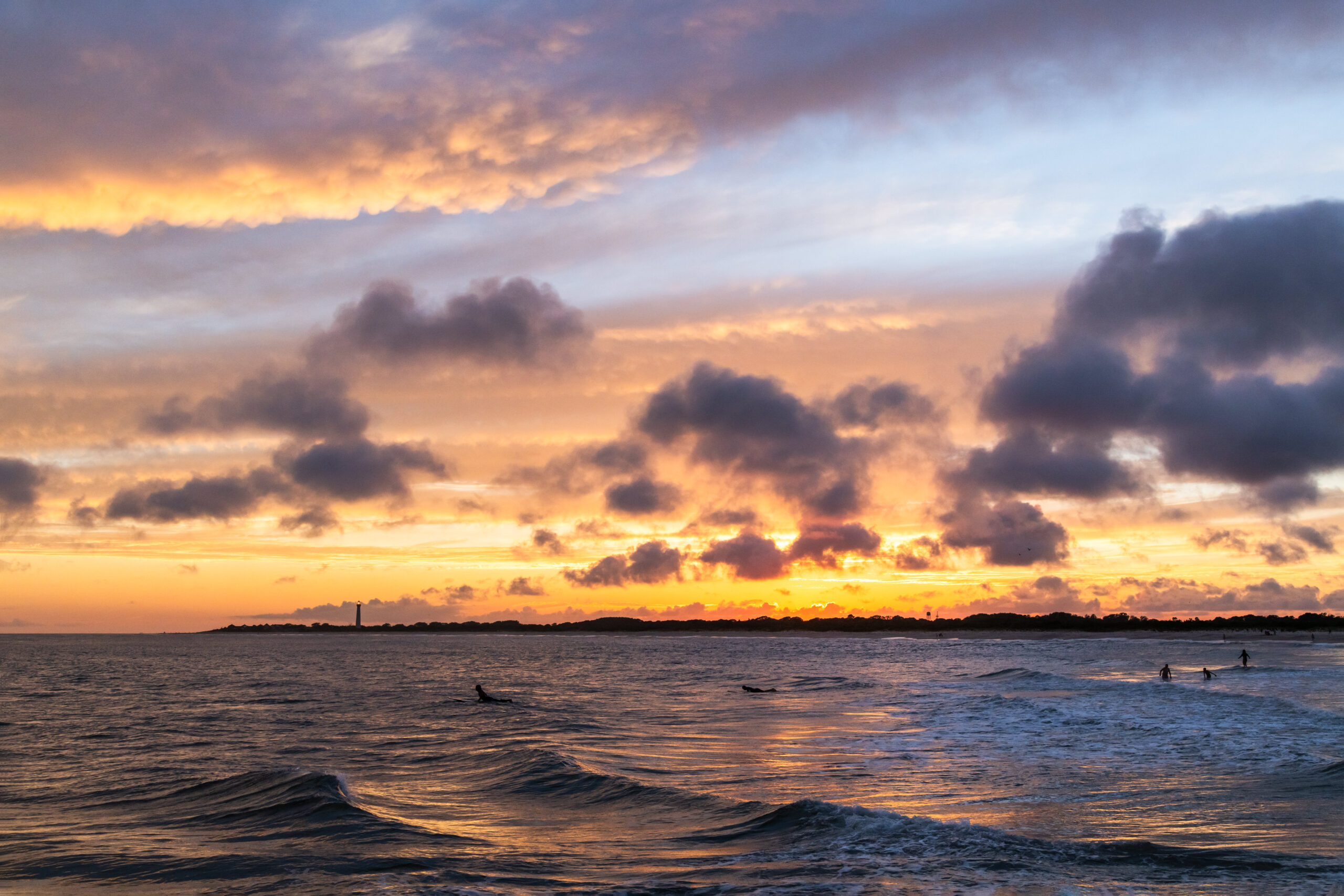 Colorful and dramatic clouds in the sky at sunset with waves rolling in and the Cape May Lighthouse in the distance