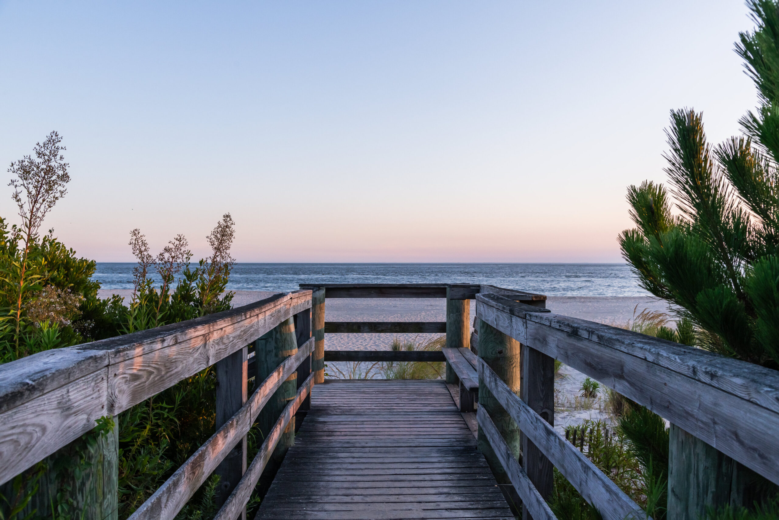 A wooden path to the beach at sunset with a clear blue and pink sky