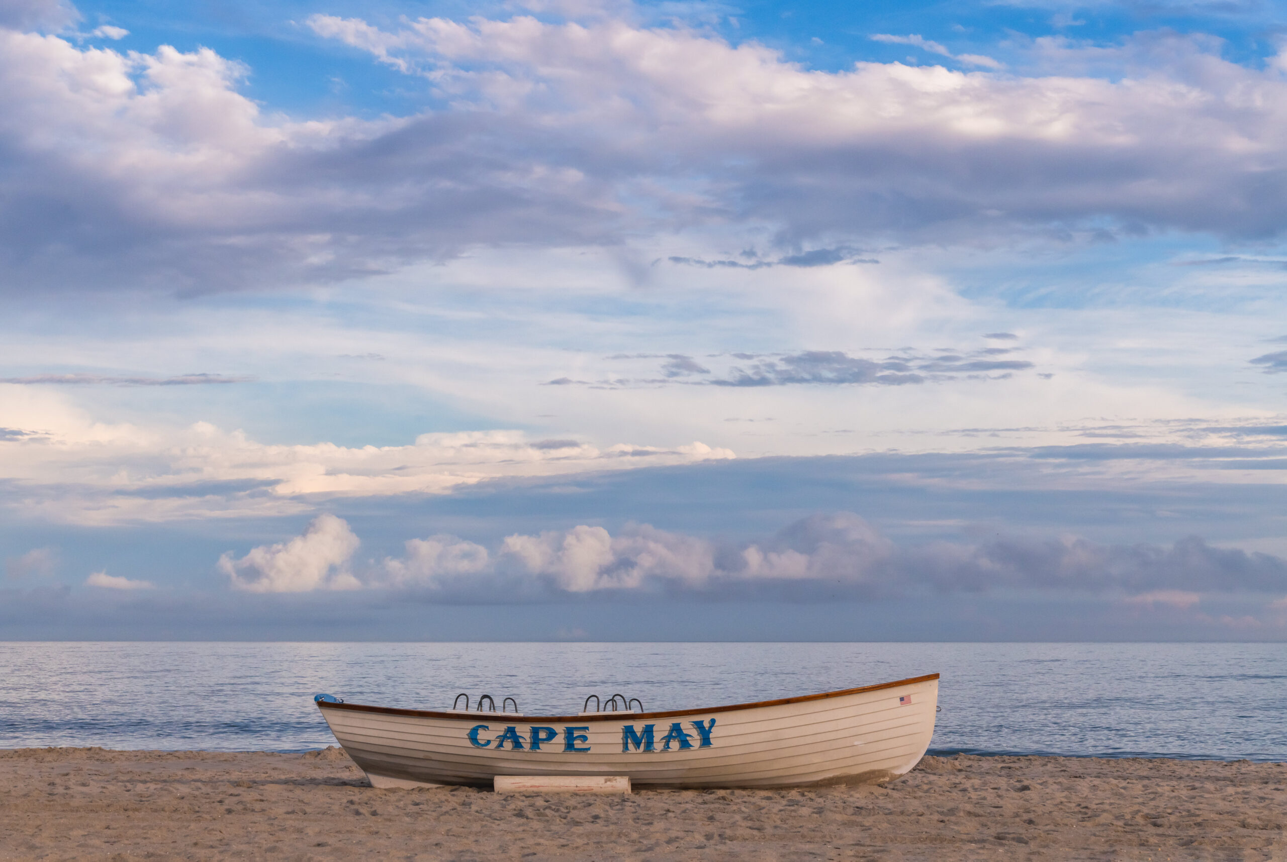 A Cape May lifeguard boat on the beach in front of a flat crystal clear ocean, and wispy blue and white clouds in the sky