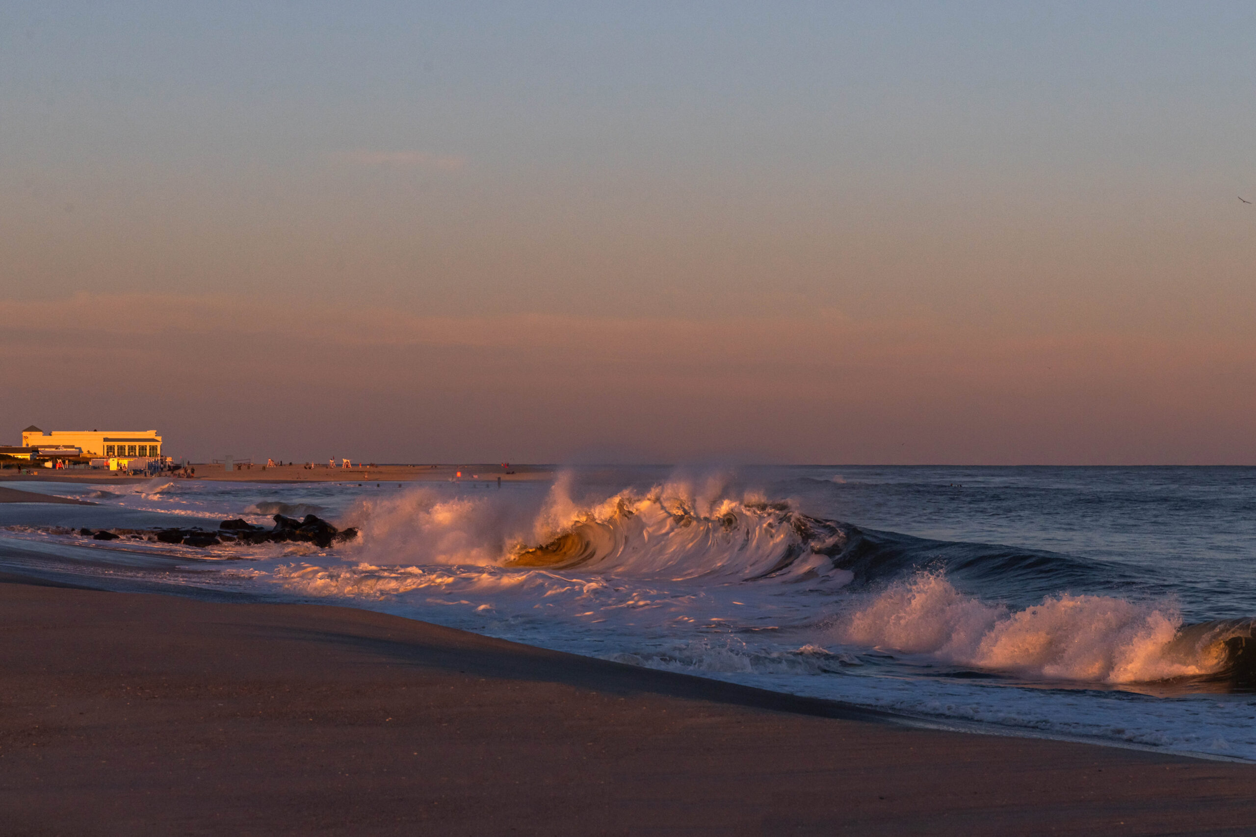A wave crashing at sunset with a clear sky, and Convention Hall in the distance