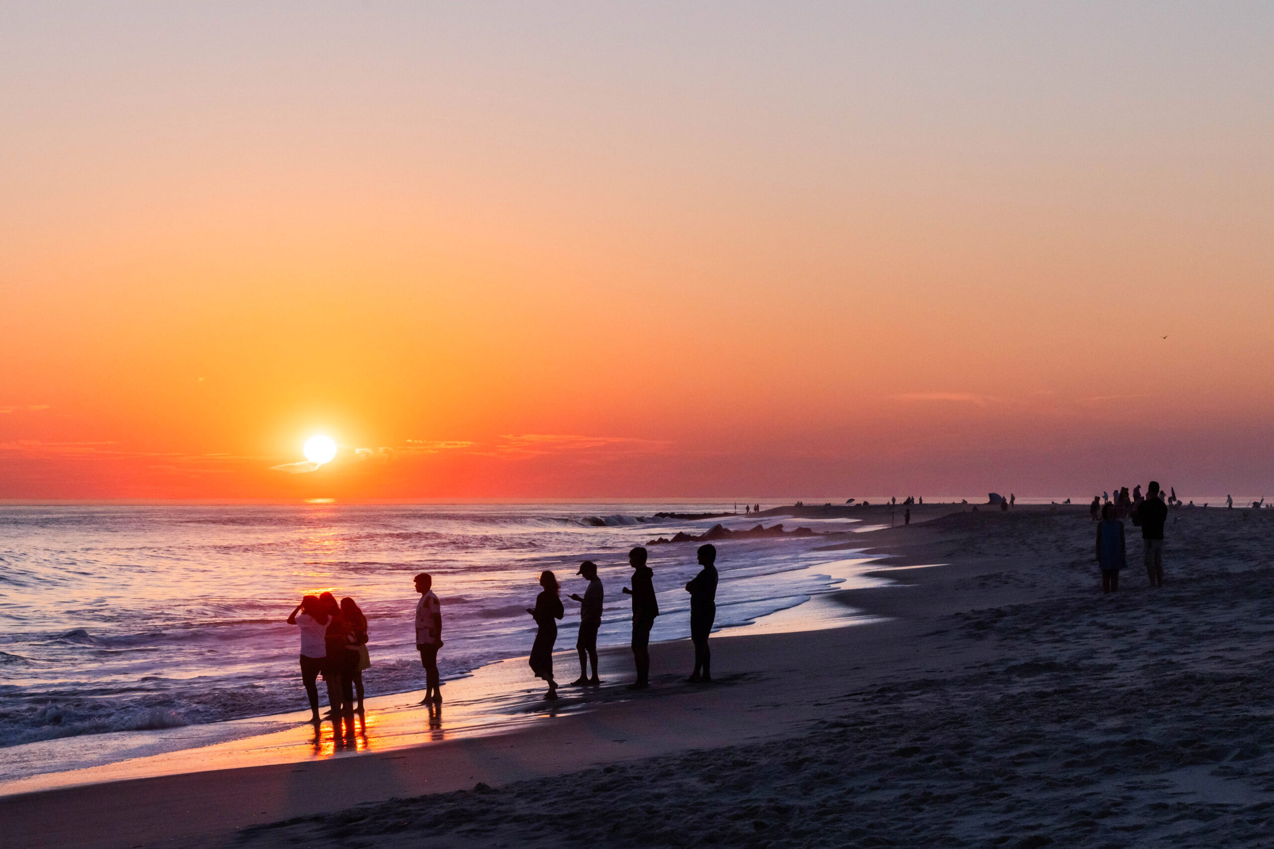 People gathered on the beach and by the ocean at sunset with a clear sky