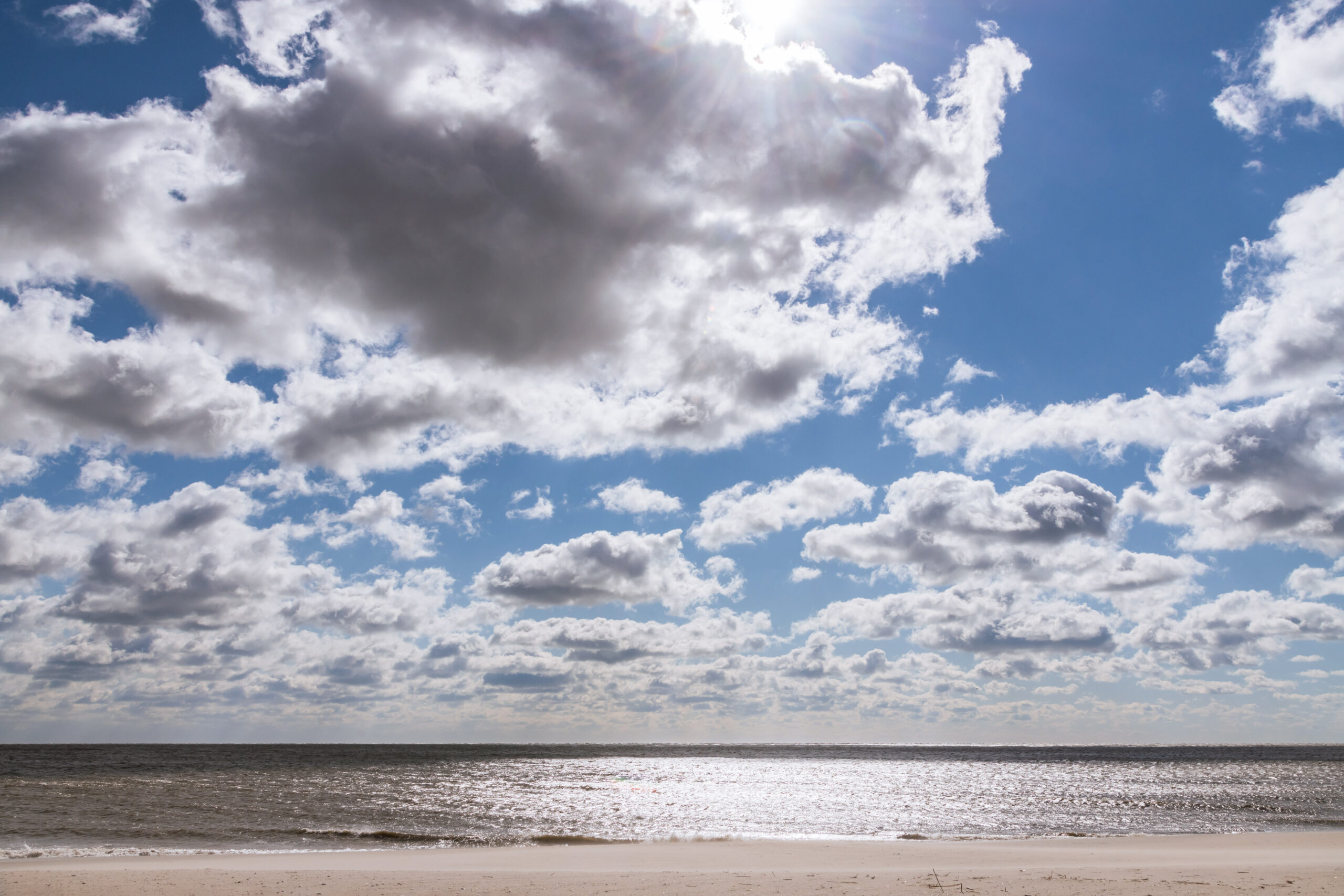 Big puffy clouds in a blue sky with the sun shining on the ocean