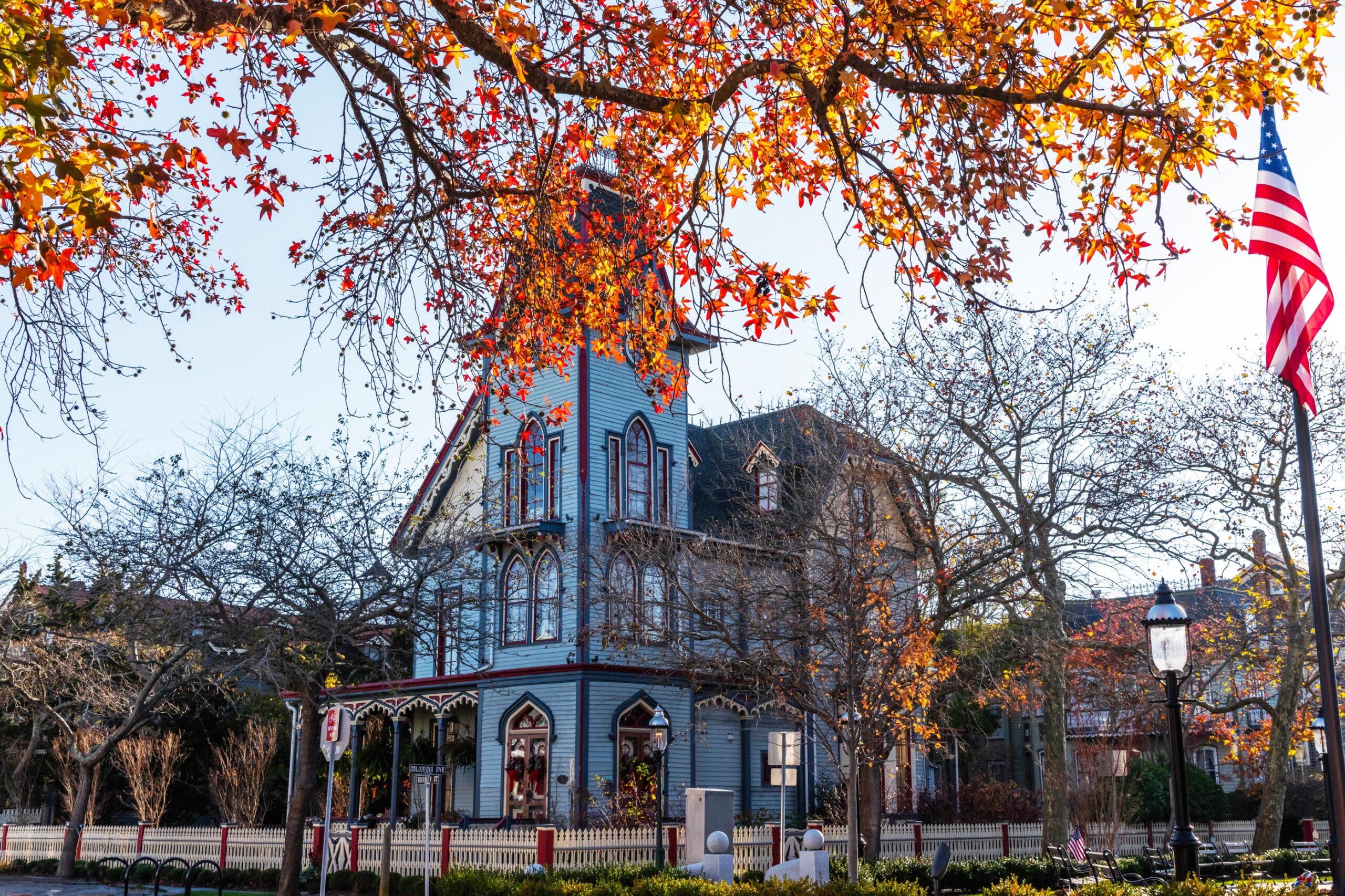 Red and orange leaves on a tree in front of The Abbey and an American Flag on a sunny day.