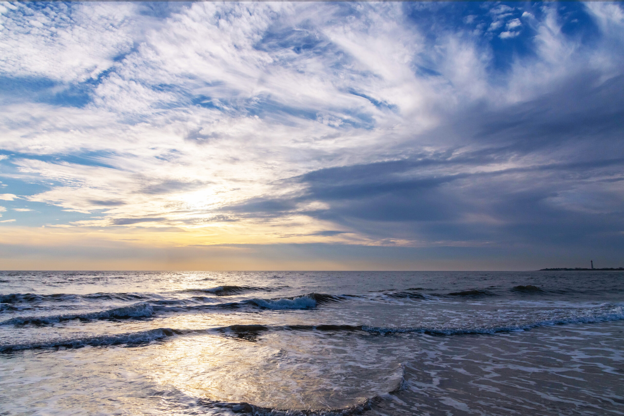 Wispy thin blue and yellow clouds in the sky with small waves in the ocean