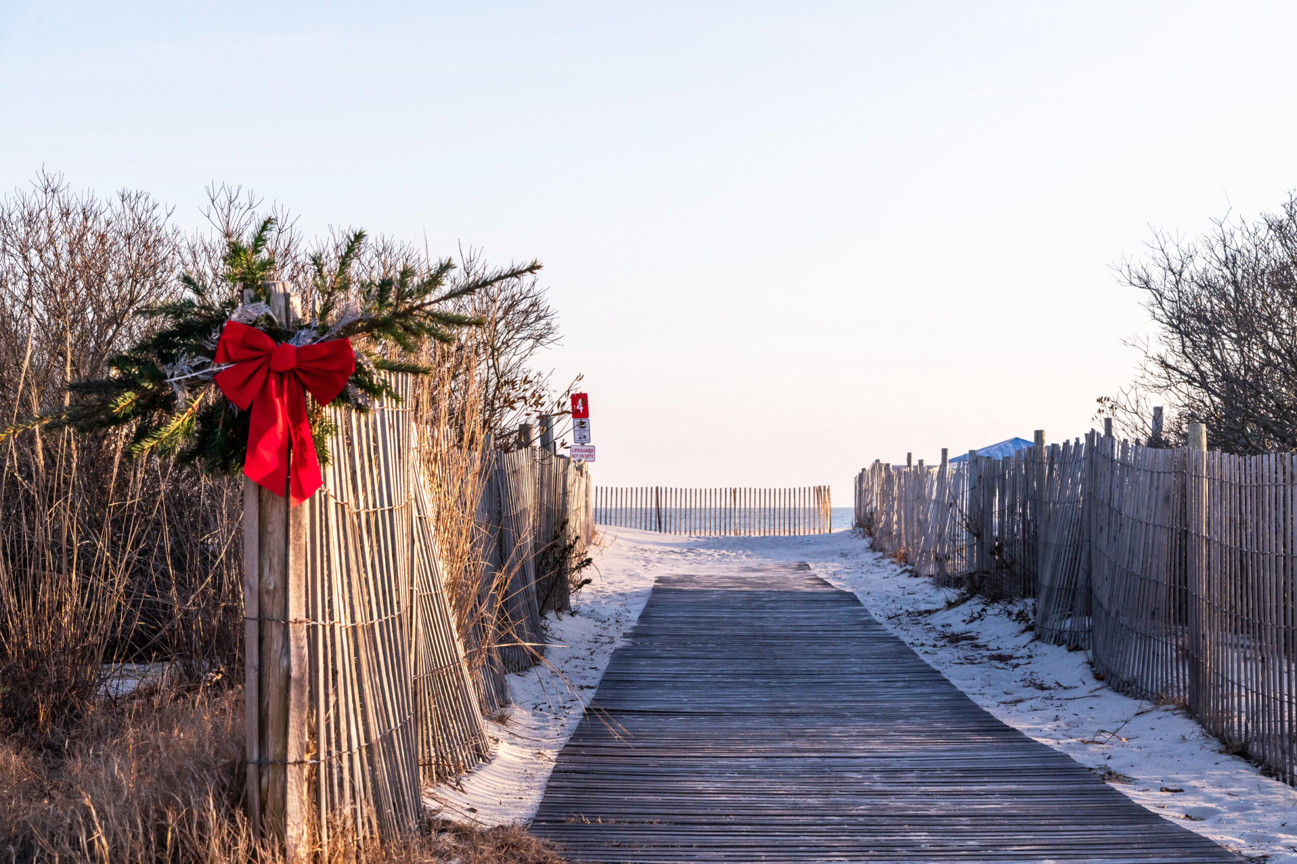 Evergreen and a red bow hung on the fence on the path leading to the beach on a sunny afternoon