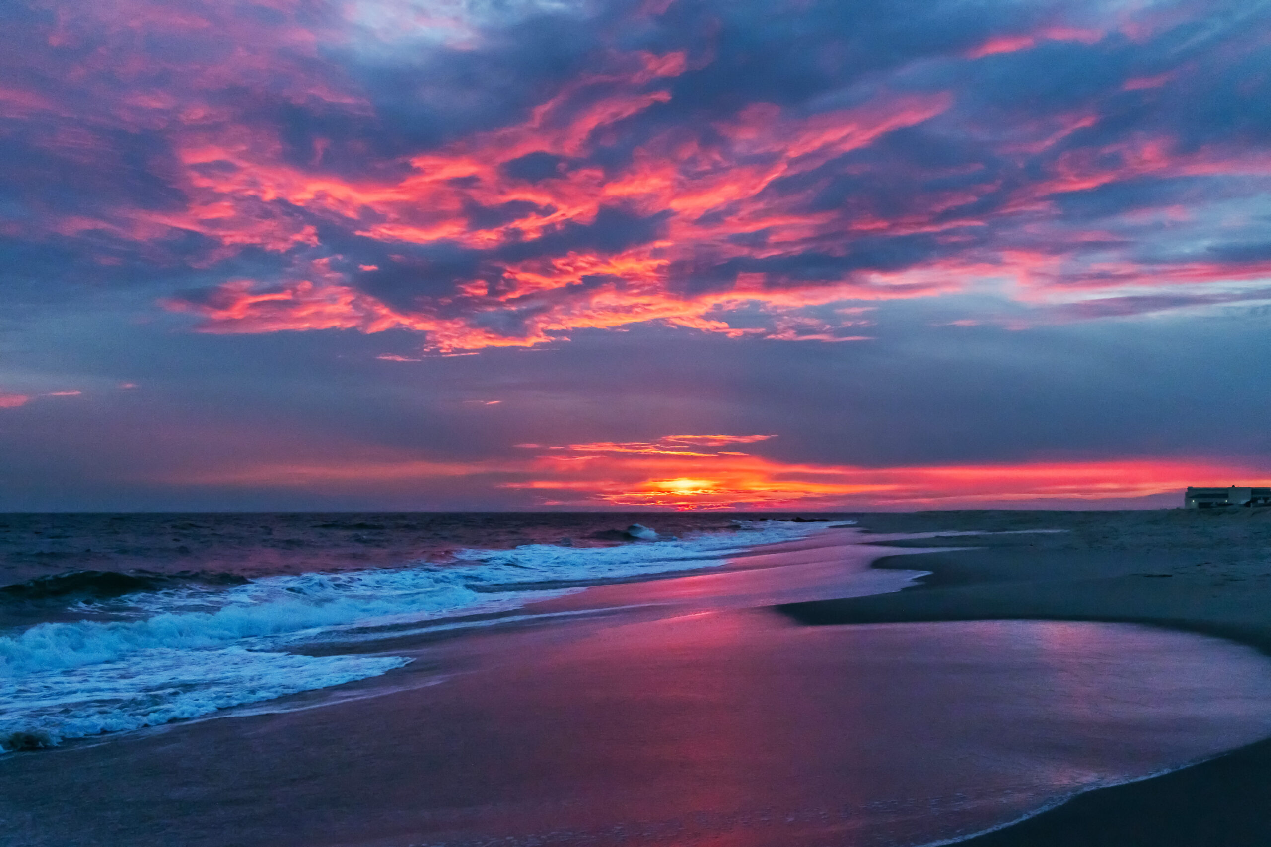 Pink and blue clouds in the sky reflected in the ocean and sand at sunset