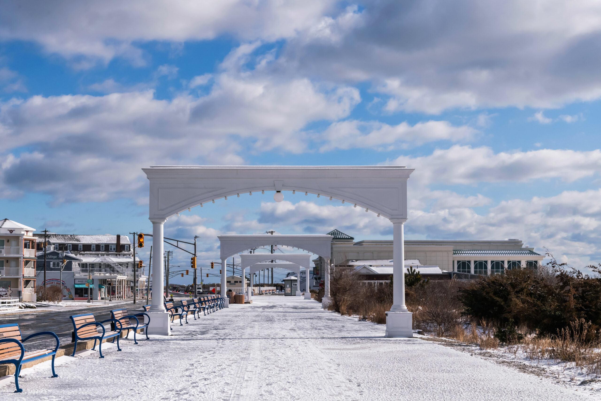 Snow on the promenade under the Cape May Arches. There are puffy clouds in a blue sky.