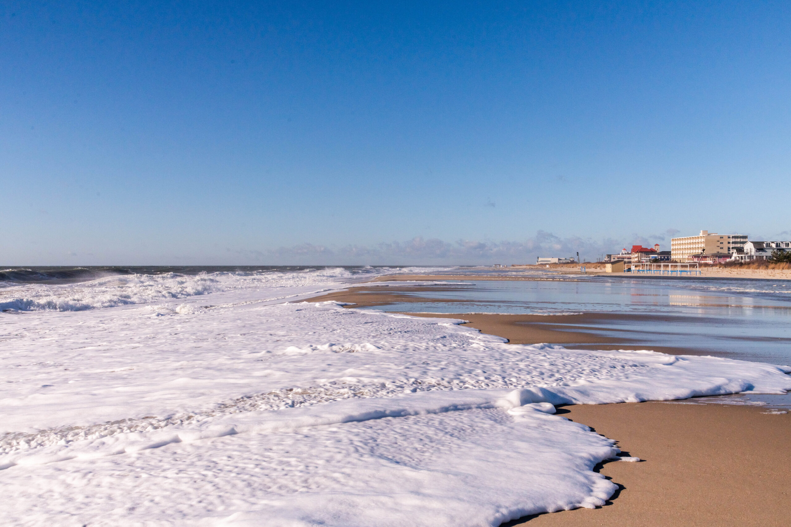 The ocean coming up high on the beach with a bright blue sky