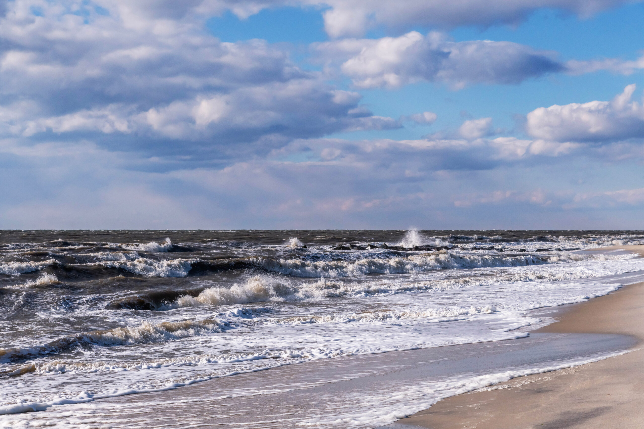 Puffy clouds in a blue sky with rough waves crashing on the ocean