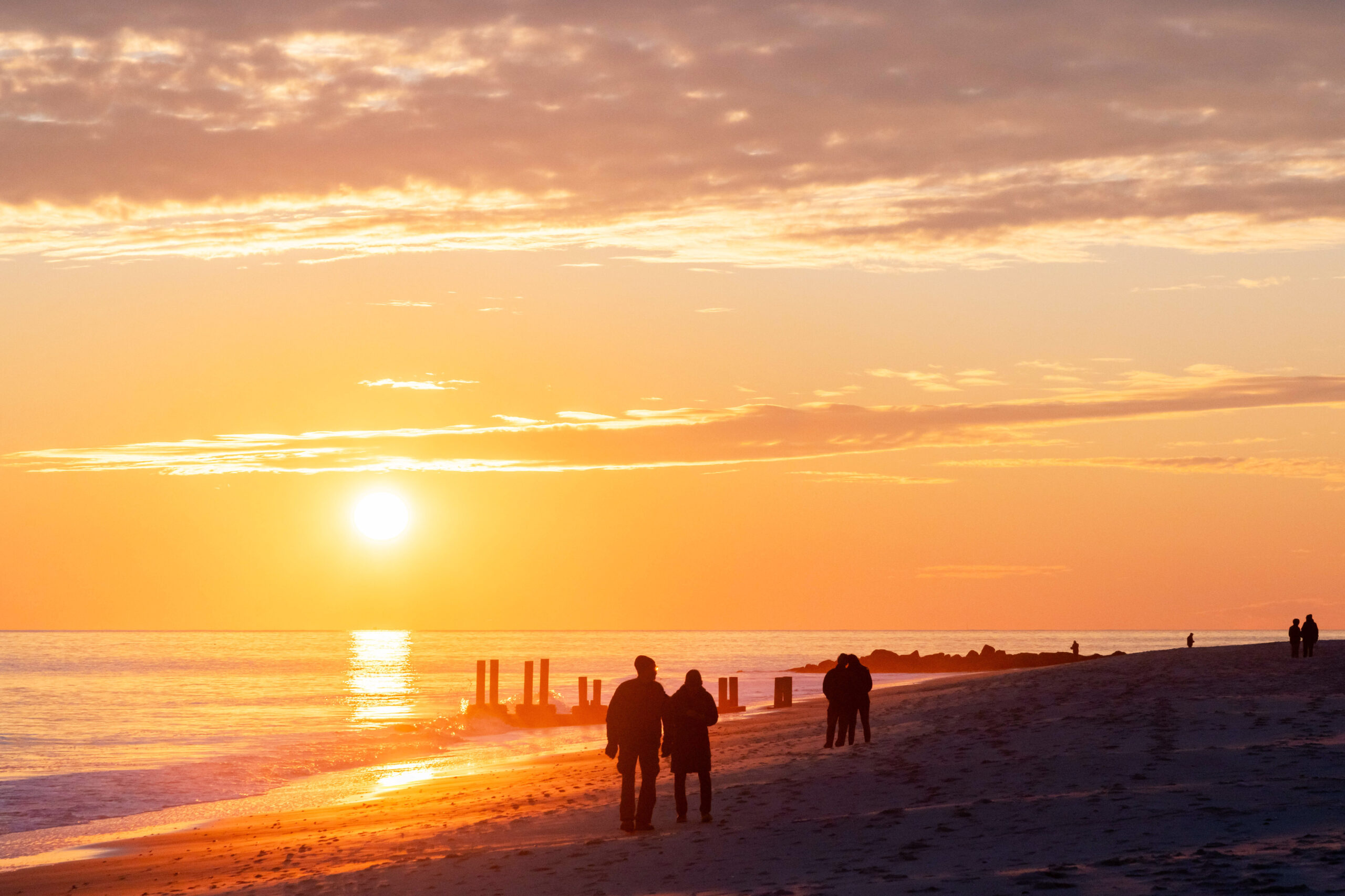 Couples walking on the beach with a few thin clouds at the sky and the setting sun shining brightly