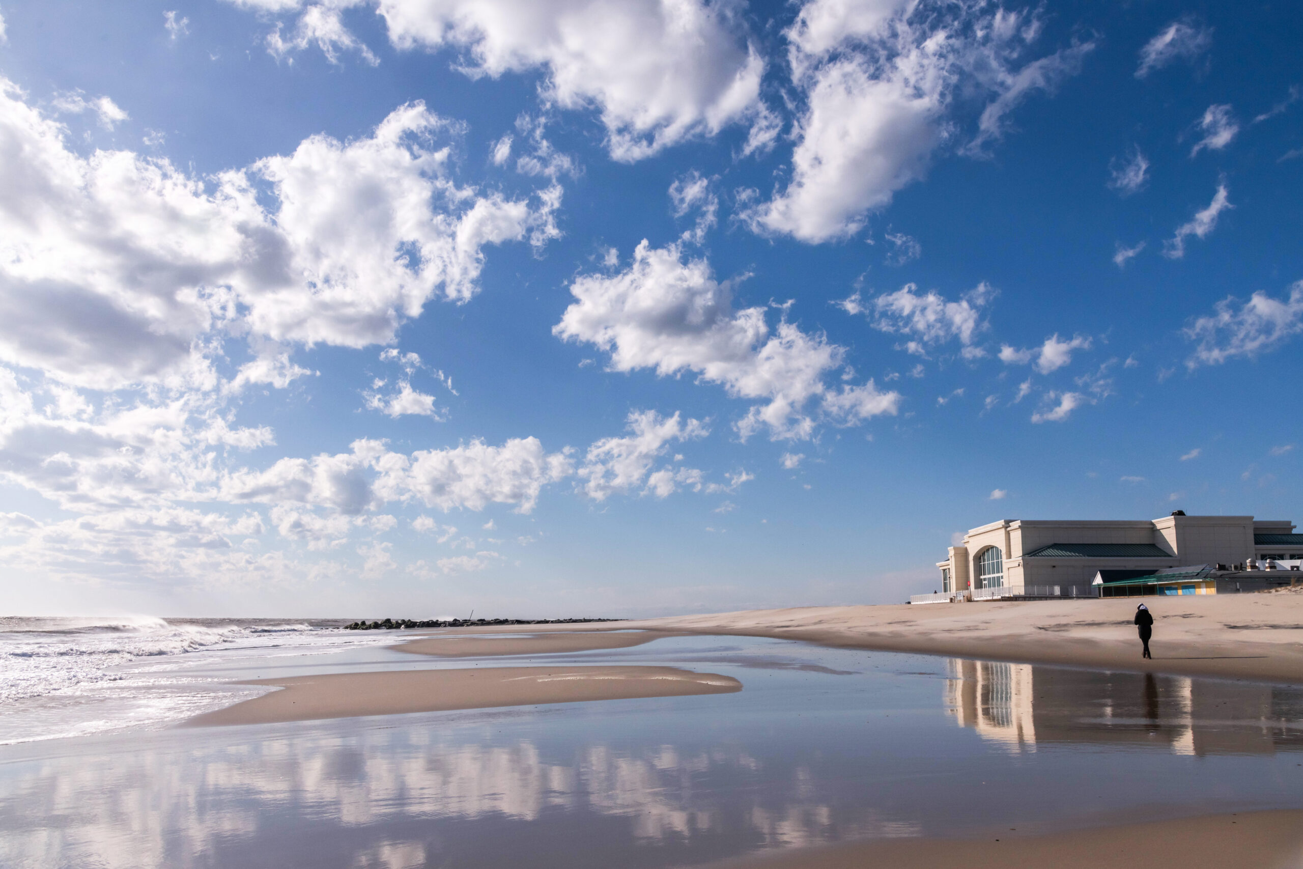 Convention Hall and the blue sky with puffy white clouds reflected in the ocean and sand