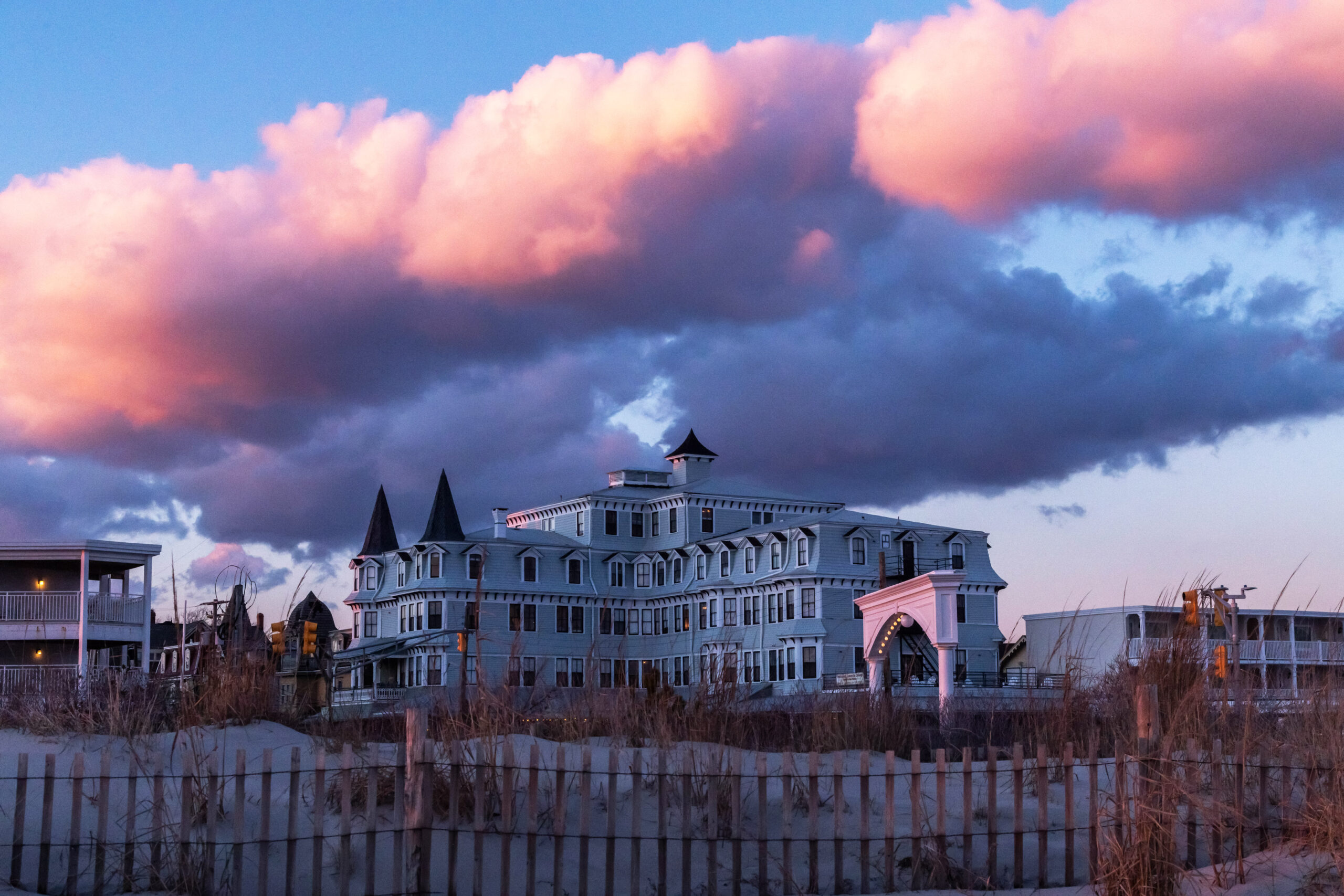 A view of the Inn of Cape May from the beach with a big puffy pink and purple cloud in the sky.