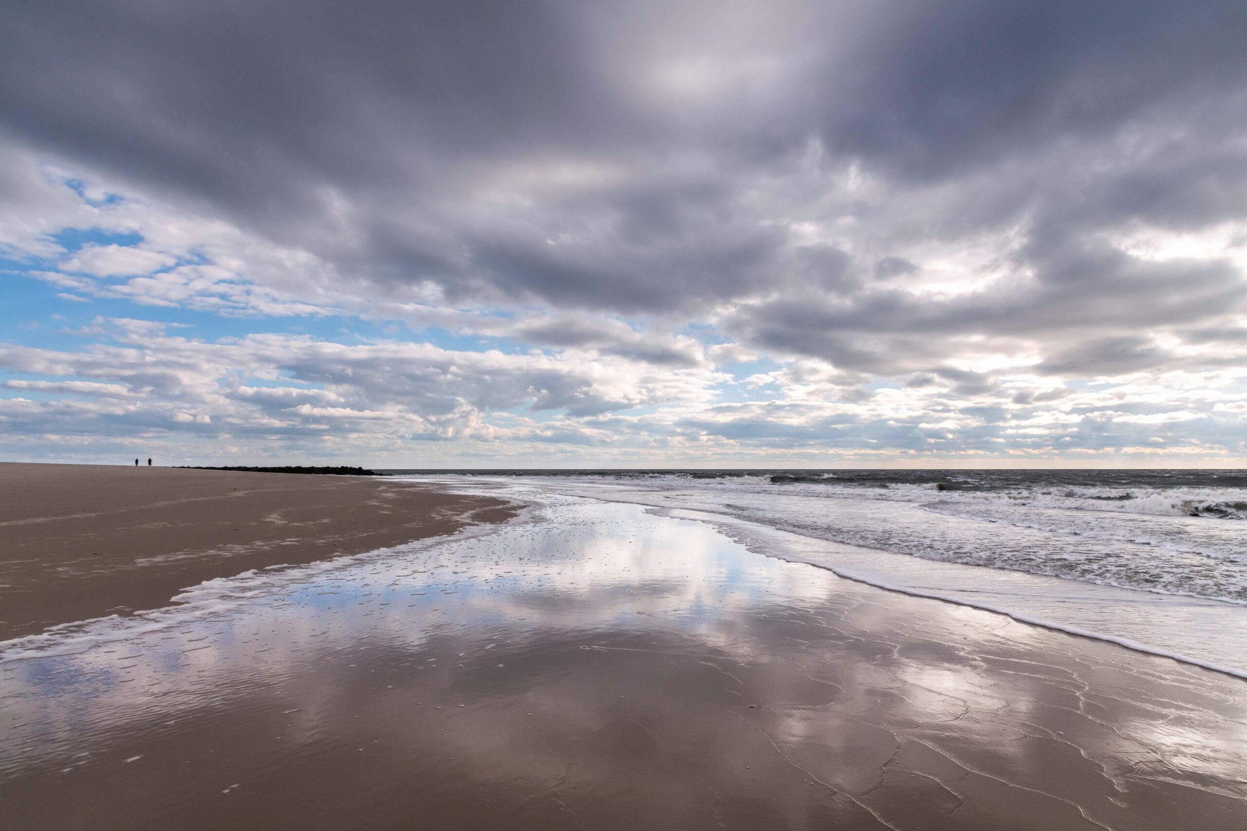 Puffy dramatic clouds in a blue sky reflected in the beach and ocean