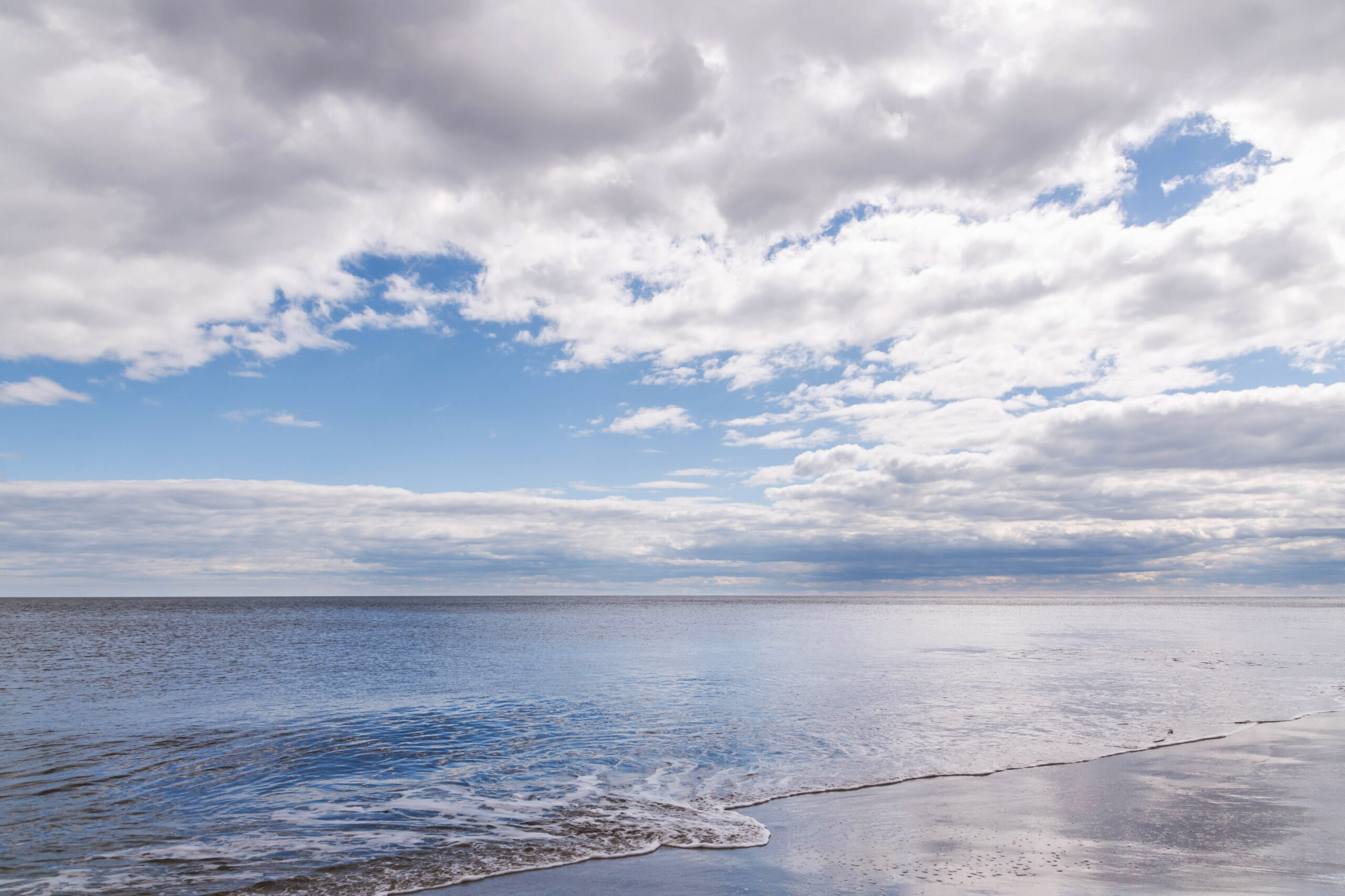 Puffy white and blue clouds in a blue sky reflected in a glassy flat ocean