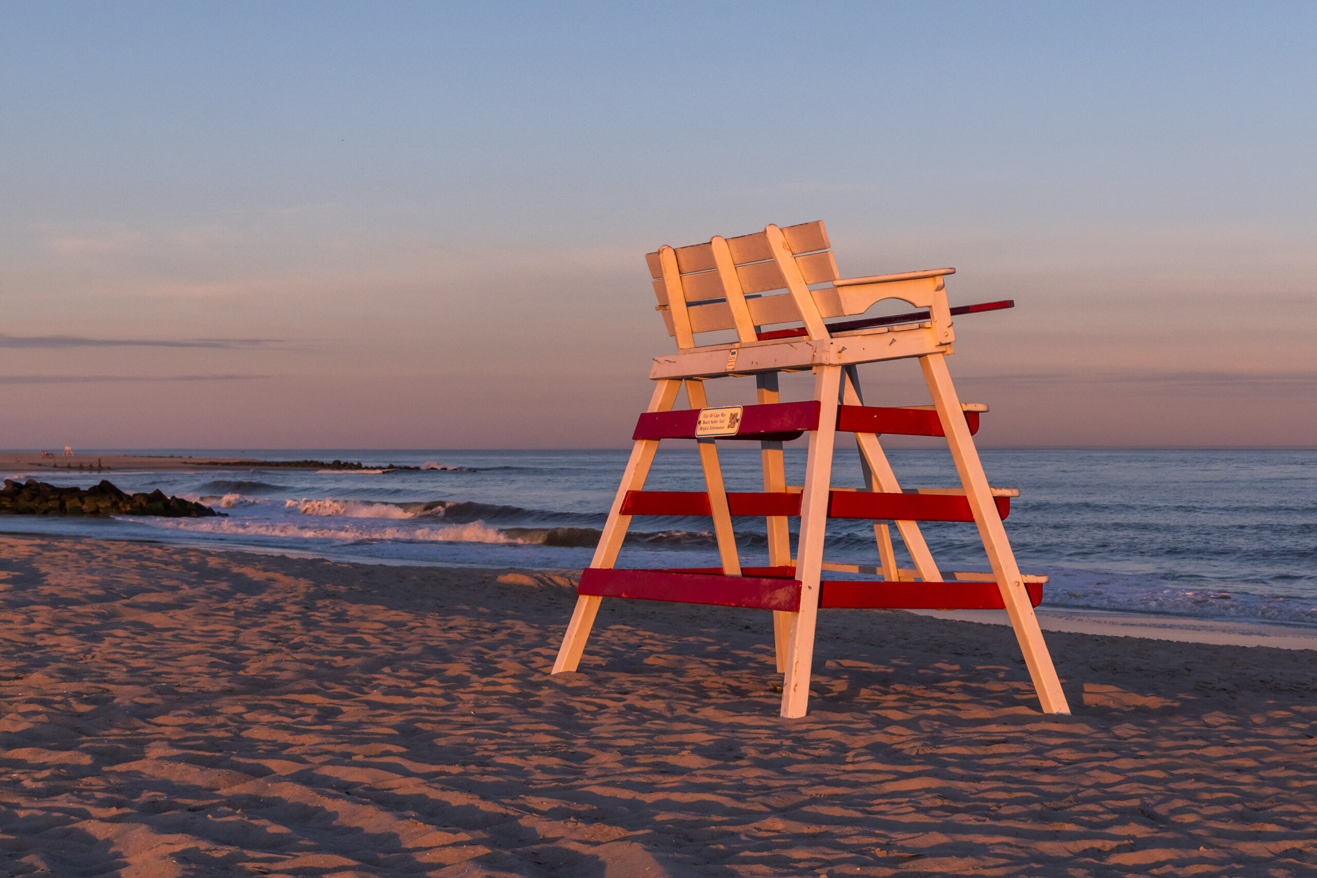 A red and white lifeguard stand on the beach at sunset with waves crashing in the ocean