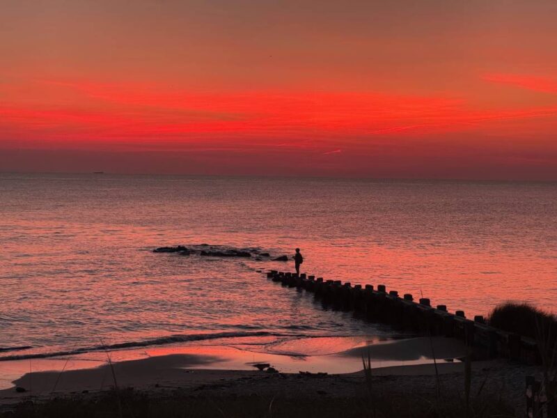 Young teen stands on jetty pier casting a pole into the Delaware Bay at twilight