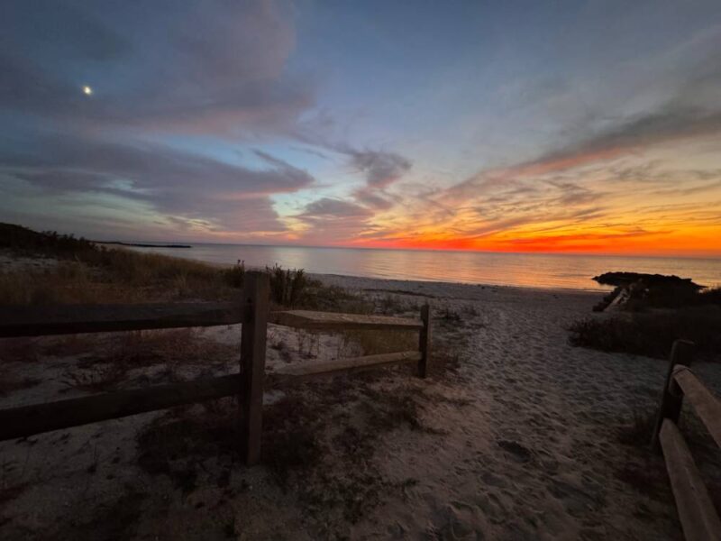 Post sunset with the moon rising and orange skies on the Delaware bay beach with a jetty and sandy walkaway