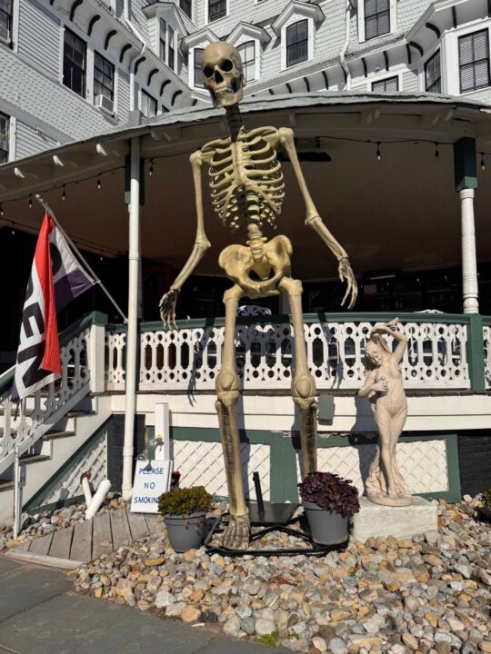 giant skeleton looms over small Victorian statue in front of the Inn of Cape May