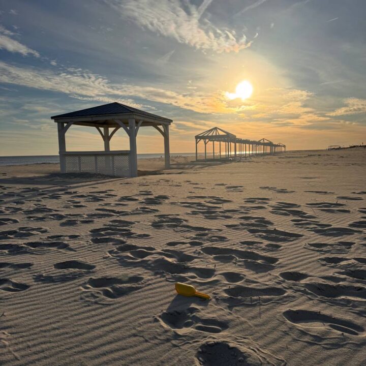 Winter Beach with bright January sun, small yellow shovel leftover from summer in the foreground, with pavilions along the coast