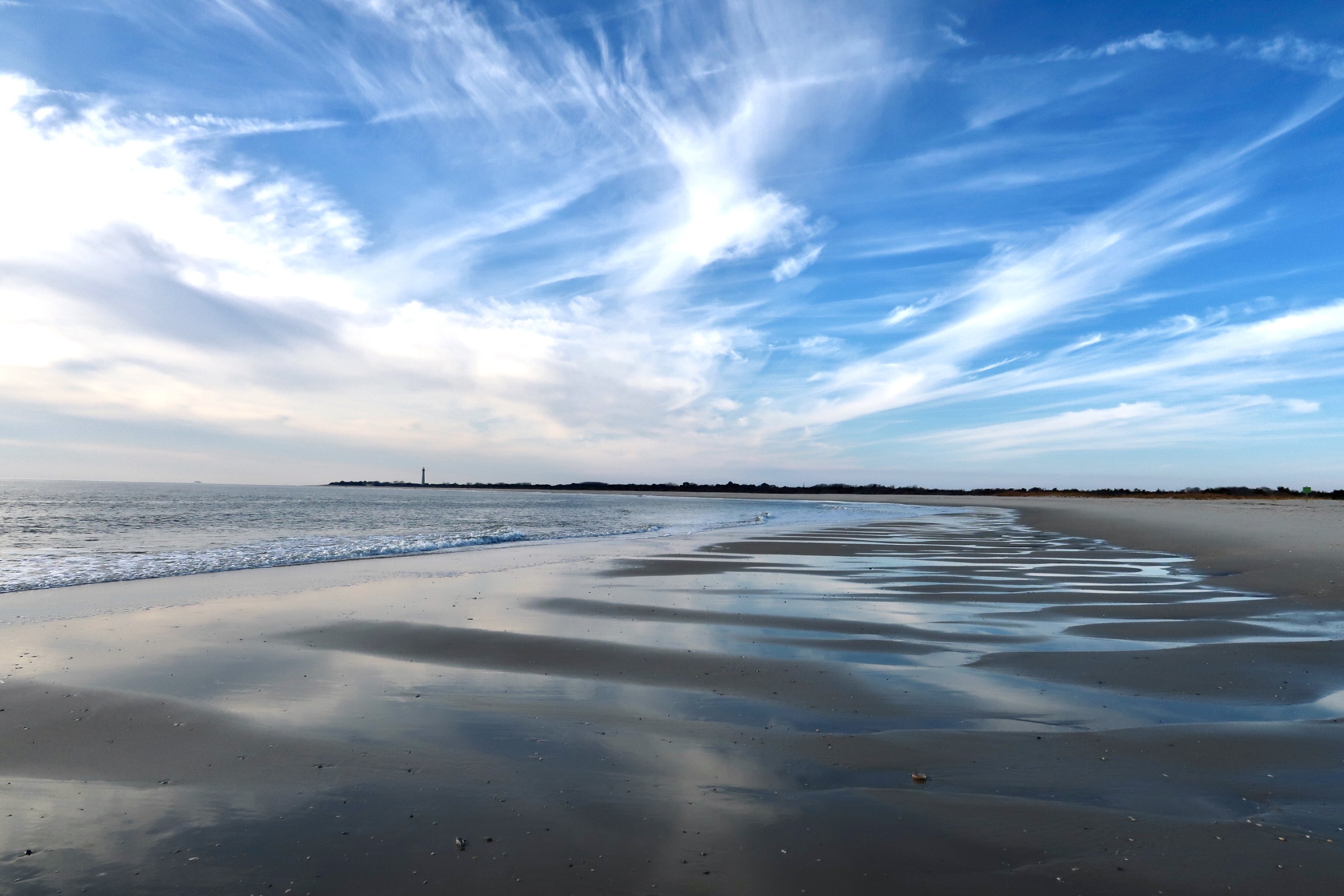 The Cove sky reflected on sand with lighthouse in background 
